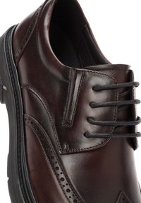 Zapato de vestir de cuero marrón con punta redonda, detalles perforados y cordones negros. Presenta una parte superior texturizada y una suela de goma duradera.