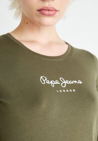 Maslinasto zelena majica od mekog materijala s okruglim izrezom i bijelim logotipom "Pepe Jeans London" na prednjoj strani.