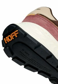 Primo piano della suola di una sneaker che mostra il battistrada nero con il logo arancione "HOFF", la parte superiore in suede rosa e la suola intermedia bianca con il testo "HOFF" in rilievo.