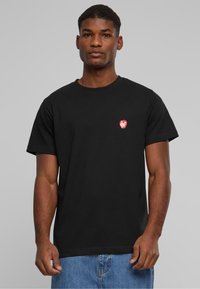 Sort bomulds t-shirt med rund hals, der har et lille rødt grafisk logo på venstre bryst. Klassisk pasform med korte ærmer.