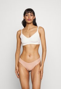 Bralette leggero bianco con design a V, abbinato a mutandine basse in pesca morbido, caratterizzate da cuciture minime e dettagli del logo.