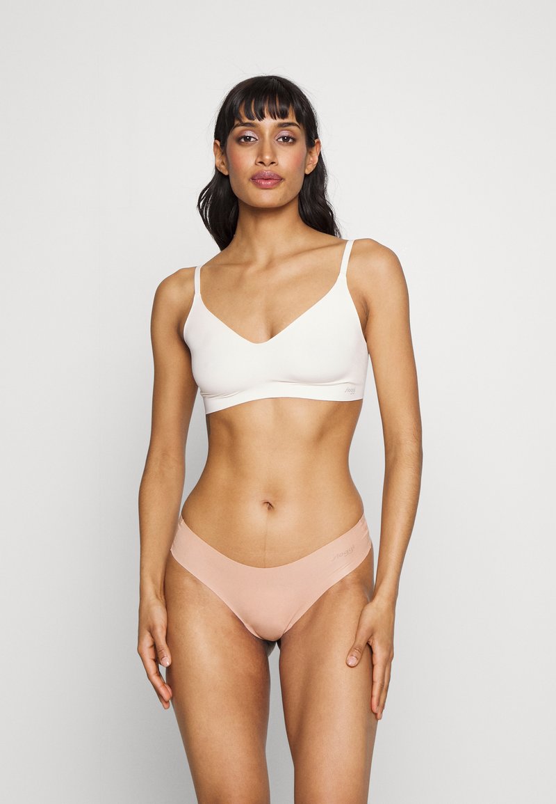 Bralette leggero bianco con design a V, abbinato a mutandine basse in pesca morbido, caratterizzate da cuciture minime e dettagli del logo.