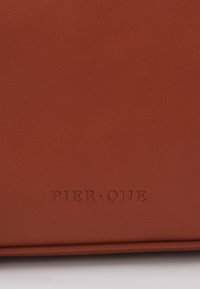 Brun lædertaske med en struktureret overflade. Præget "PIER • ONE" logo i midten, med rene kanter og et minimalistisk design.