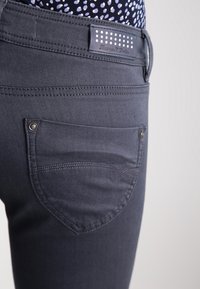 Jeans gris foncé au design ajusté, avec une poche arrière décorative, des détails de couture visibles et une étiquette en tissu avec des points.