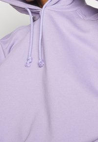 Hellblaues Sweatshirt mit Kapuze, Zugbändern mit Knoten und einer weichen Textur, von der Schulter abwärts gezeigt.