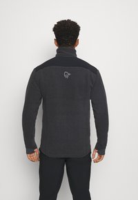 Giacca in pile grigio scuro con colletto alto e accenti neri sulle spalle. Presenta una finitura testurizzata e un logo sulla parte posteriore.