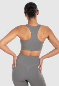 Grijze sportbh met een racerback ontwerp, een gladde textuur en een strakke pasvorm, gecombineerd met hoge grijze leggings.