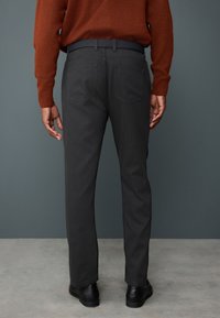 Ciemnoszare spodnie o prostym kroju, wykonane z bawełny, z dwoma tylnymi kieszeniami. Model ma na sobie brązowy, fakturowany sweter oraz czarne buty.