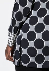 T-shirt à manches longues avec un motif circulaire bleu marine et gris, doté d'un poignet à pois et de fentes sur les côtés pour plus de détail.