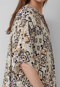 Kimono-stijl top met een geometrisch patroon in beige, bruin en zwarte tinten. Gemaakt van lichte stof met een comfortabele pasvorm en brede mouwen.