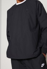 Black Nike sweatshirt with a crew neckline, ribbed cuffs, and embroidered logo on the chest. Lightweight material with a smooth texture.