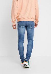 Ljust blå skinny jeans med en urtvättad textur, ihop med en persikofärgad sweatshirt, och färgglada sneakers med inslag av blått, orange och grönt.