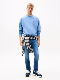 Lyseblå hettegenser med ribbede mansjetter, blå jeans og flerfargede joggesko. Rutete skjorte knyttet rundt livet.
