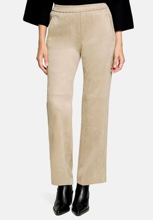 Beige bukser med vidde ben og elastisk talje, forlommer, båret med sorte støvler med spids snude og en sort top.