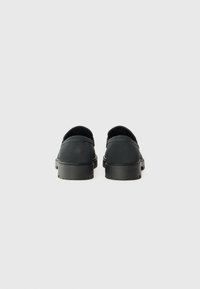 Sorte sko med en glatt skinnoverdel, rund tå og lav gummisåle. Designet har minimalt med sømmer og en uformell slip-on stil.