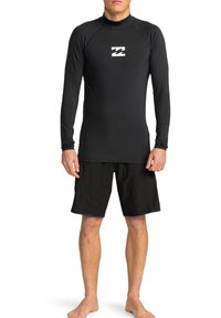 Rash guard negro de manga larga con cuello alto y logo en el pecho, combinado con bañadores negros. Tejido suave y elástico.