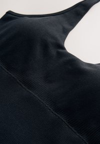 Canotta sportiva nera in tessuto liscio ed elastico, con design a incrocio sulla schiena e cuciture piatte per il massimo comfort. Senza motivi o decorazioni aggiuntive.