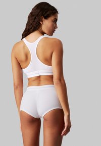 White ribbed sports bra with a racerback design and white elastic band, paired with matching ribbed shorts featuring a wide waistband.