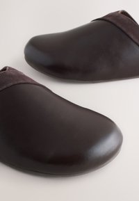 Paire de sabots en cuir marron foncé à enfiler avec une bordure en suède doux sur une surface claire.