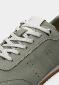 Αθλητικό παπούτσι από σουέντ σε ανοιχτό πράσινο χρώμα με λευκά κορδόνια, διάτρητο σχέδιο, κυκλικό ασημένιο οφθαλμό και ταμπά λαστιχένια σόλα. Το λογότυπο είναι τυπωμένο στην πλευρά.