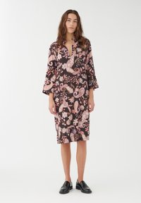 Svart klänning med ett paisley- och blommönster i rosa och vita nyanser. Har krage och 3/4-långa klockärmar. Bärs med svarta loafers.