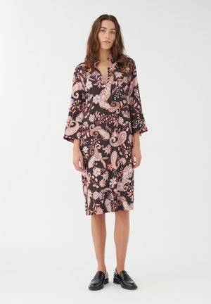 Abito nero con un motivo paisley e floreale in tonalità di rosa e bianco. Presenta un colletto e maniche a campana 3/4. Indossato con mocassini neri.