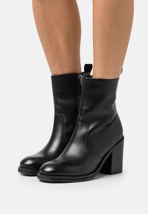 Bottines en cuir noir avec une texture lisse, dotées d'un talon bloc, d'une fermeture éclair sur le côté et d'un design de bout rond.
