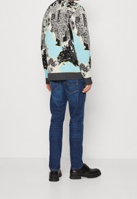 Maglione multicolore con motivi astratti, polsini grigi, indossato con jeans blu scuri e stivali neri, in un classico design in denim.