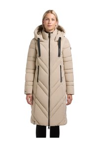 Beige gewatteerde jas met een capuchon, voorzien van chevron-stiksel, zwarte rits en trekkoorden. Lange, aansluitende mouwen en zijzakken.