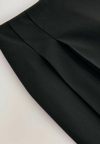 Jupe noire plissée, faite d'un tissu doux. Présente un design épuré et une surface texturée, mettant en valeur la structure et la forme.