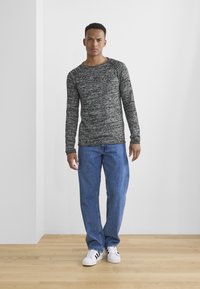 Lichte, lange mouwen, grijze gemarmerde trui met ronde hals, gecombineerd met blauwe rechte jeans en witte sneakers met zwarte strepen.
