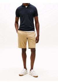 Tummansininen polo-paita klassisella kauluksella, beiget shortsit ja valkoiset lenkkarit. Polossa on pieni brodeerattu logo rinnassa.