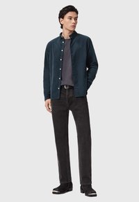 Camicia in velluto a coste di colore verde scuro, t-shirt grigia, jeans neri e stivaletti con accenti argentati. Design slim-fit, texture morbida e chiusura con bottoni.