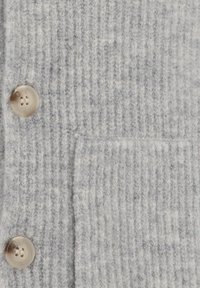 Teksturowana szara dzianina z pionowymi prążkami, z wyraźną kieszenią naszywaną oraz dużymi, okrągłymi, beżowymi guzikami.