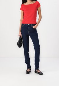 Červený krátký rukáv top spárovaný s tmavě modrými kalhotami s vysokým pasem. Černá kabelka a černé baleríny s detaily pro vyvrtání dokreslují vzhled.