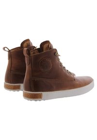 Zapatos de cuero marrón de caña alta con suelas de goma gris, acentos texturizados y una etiqueta con el logotipo en el lado exterior. Cuentan con cordones y costuras marrones.