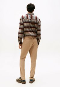 Multikleurige gestreepte shirt met tinten bruin, blauw en beige, gecombineerd met beige broeken en grijze sneakers met blauwe accenten.