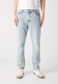 Světle modré džíny z denimu se střihem rovného nohavice, obsahující zapínání na knoflík a zip, boční kapsy a slabé vybledlé detaily.
