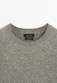 Maglione grigio lavorato a maglia con scollatura rotonda, caratterizzato da un tessuto testurizzato e un'etichetta con la scritta "Massimo Dutti". Materiale 100% cotone.