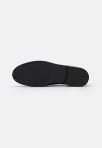 Semelle noire avec une surface lisse et texturée. Présente un logo de marque et des bords flexibles. Conçue pour le confort et la stabilité.