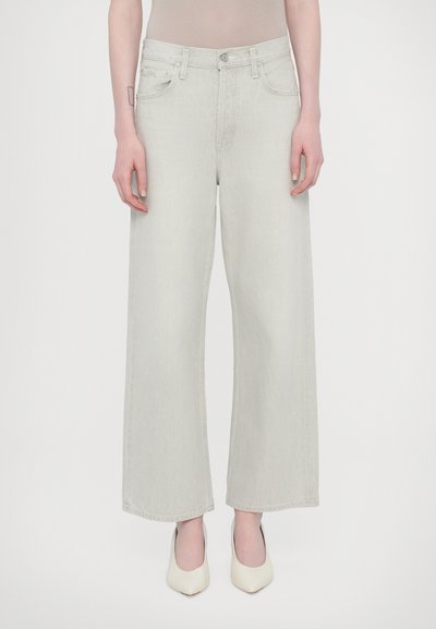 Lichtgrijze wijdlopende spijkerbroek van denim, met een hoge taille, voorzakken en een knoopsluiting. Gepaard met beige puntige hakken.