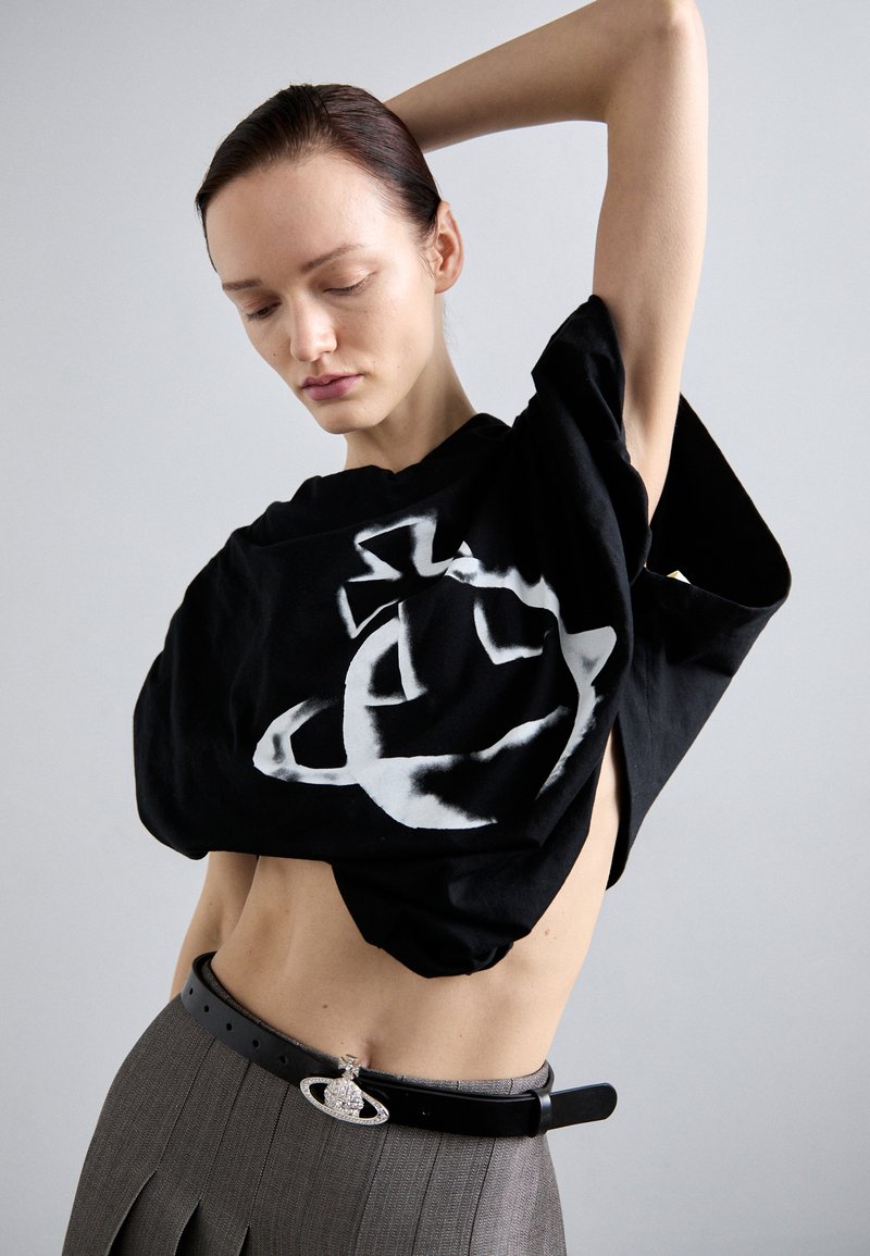 T-shirt oversized preto com design gráfico branco, apresentado com uma saia plissada cinza e um detalhe de cinto. Tecido macio com um corte solto.