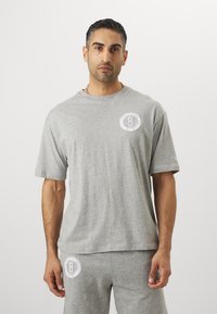Camiseta de algodón gris de manga corta con un logo redondo blanco en el área del pecho izquierdo. Corte informal con escote redondo y textura suave.