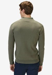 Olivgrön ribbad tröja med långa ärmar och krage. Har en texturerad tyg och en kroppsnära design, synliga sömdetaljer vid axlarna.