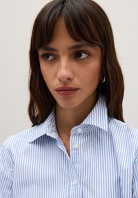 Camicia button-up a righe blu e bianche con colletto classico. Tessuto di cotone liscio con design aderente e piccoli bottoni bianchi.