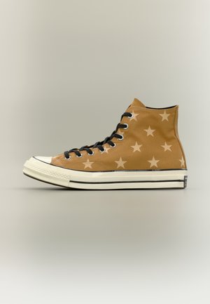 Basket montante marron avec lacets noirs et motif d'étoiles beige clair, semelle en caoutchouc blanche avec bande noire, vue de côté.