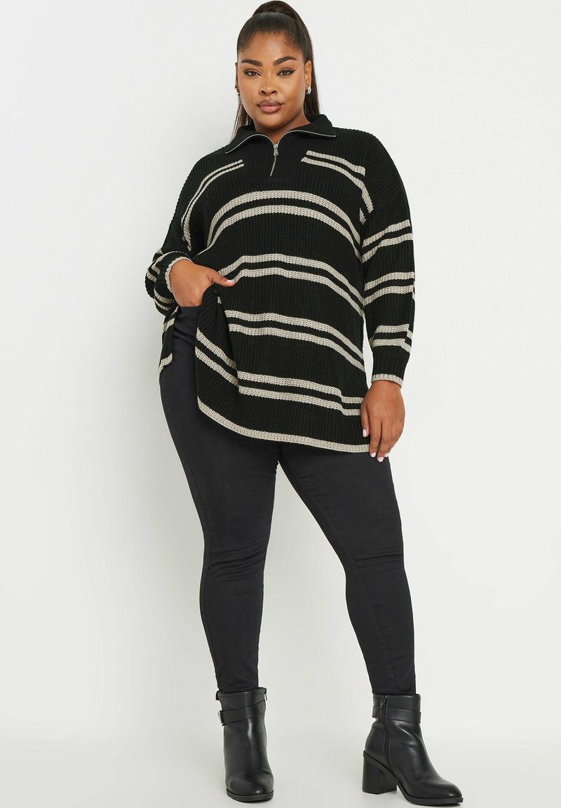 Pull en tricot rayé noir et beige avec un col zippé, présentant une coupe décontractée et des poches latérales, associé à un jean skinny noir et des bottines.