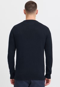 Marineblauwe gebreide trui met een ronde hals, lange mouwen en geribde manchetten. De stof heeft een gladde en gemiddelde gewicht textuur.