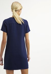 Lyhyt tummansininen mekko, joka on valmistettu sileästä kankaasta. Mekossa on lyhyet hihat, yksinkertainen kaulus ja suora siluetti, jossa on siisti helma.