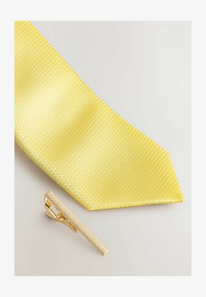 Gul slips med en struktureret vævning, sammen med en guldfarvet slipsclip med en mønstret overflade og en slank, rektangulær form.